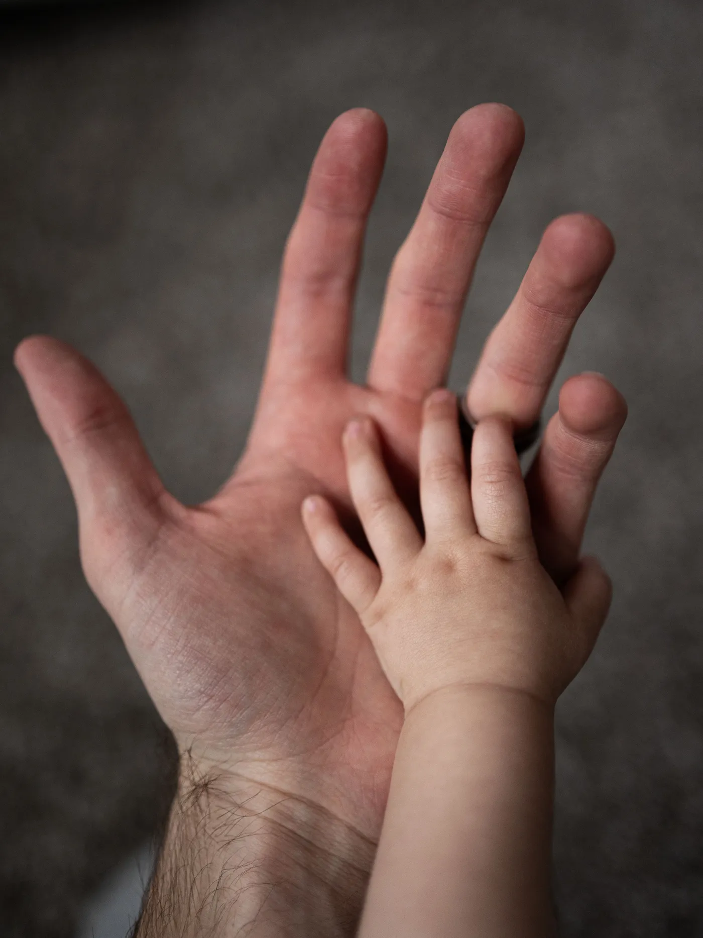 มือเด็กเล็กวางทาบอยู่บนฝ่ามือผู้ใหญ่ที่แบออก ถ่ายจากด้านบนในแสงนุ่ม